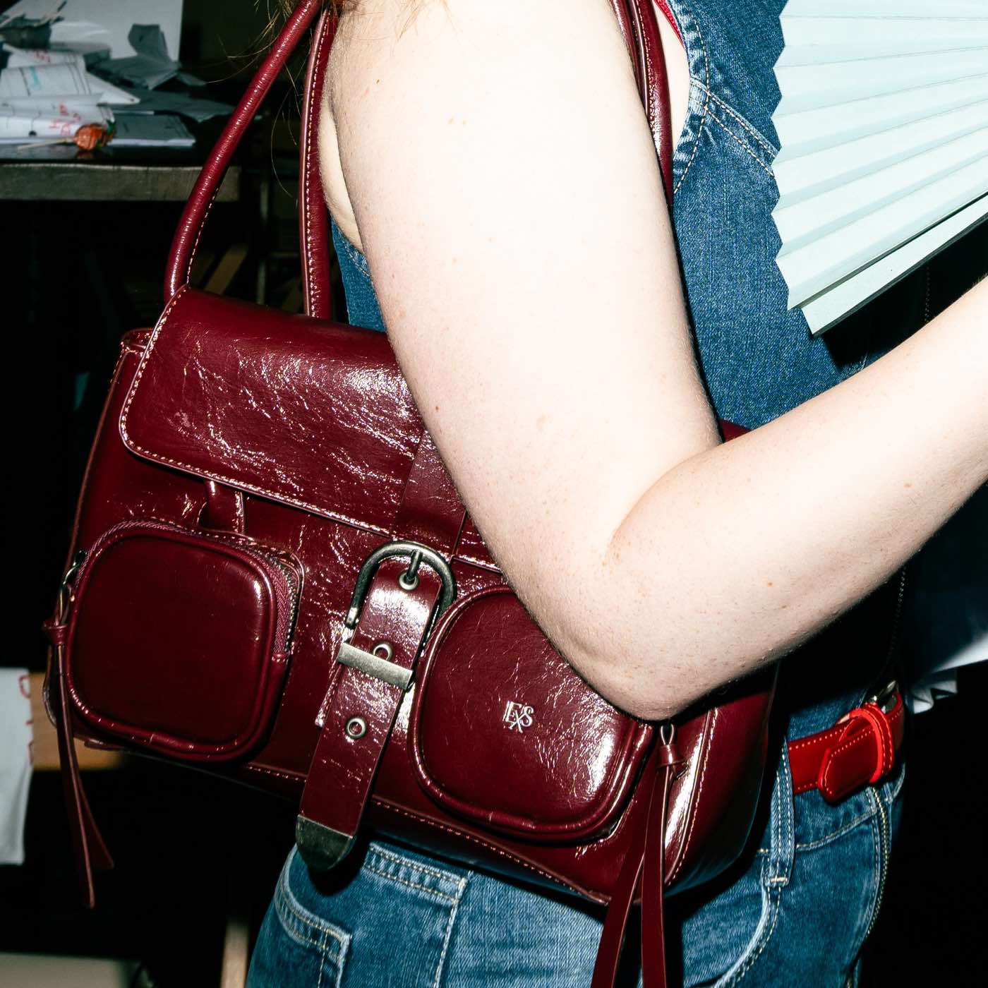 A burgundy patent leather shoulder bag worn over a denim jacket.