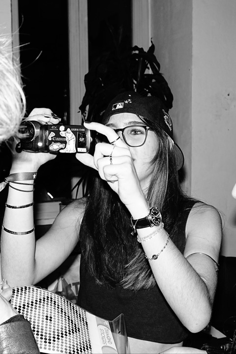 A guest in a cap and glasses filming with a small camcorder covered in stickers, two other guests close beside her.