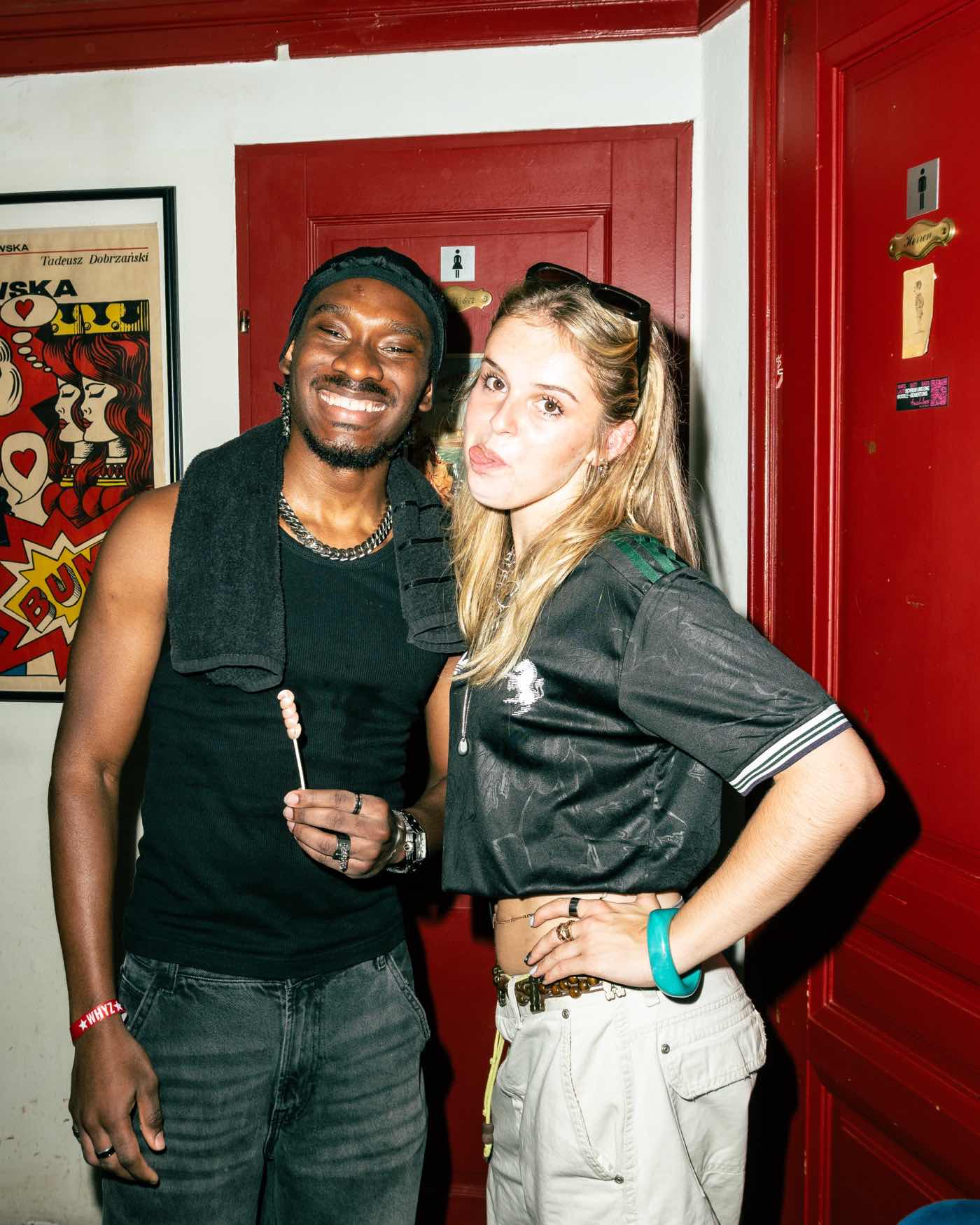 Two guests photographed with direct flash in front of a red painted door.