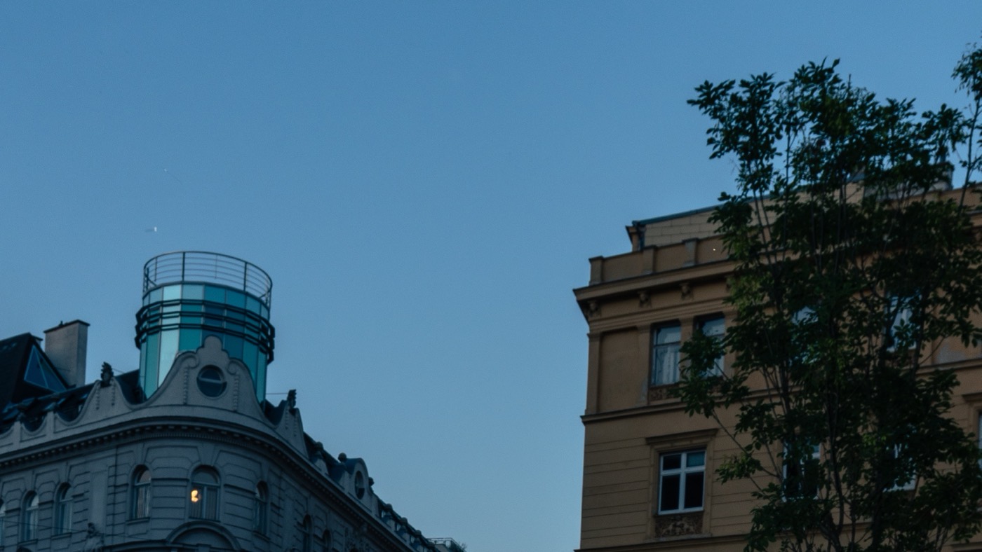 Vienna rooftops and Gruenderzeit facades against a deep blue dusk sky.